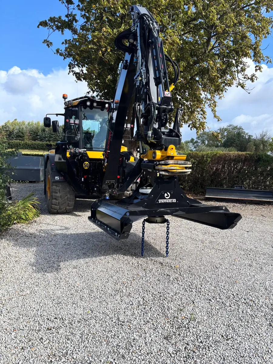 Heavy yellow and black forestry loader with a front-mounted grapple attachment on a gravel lot under a blue sky